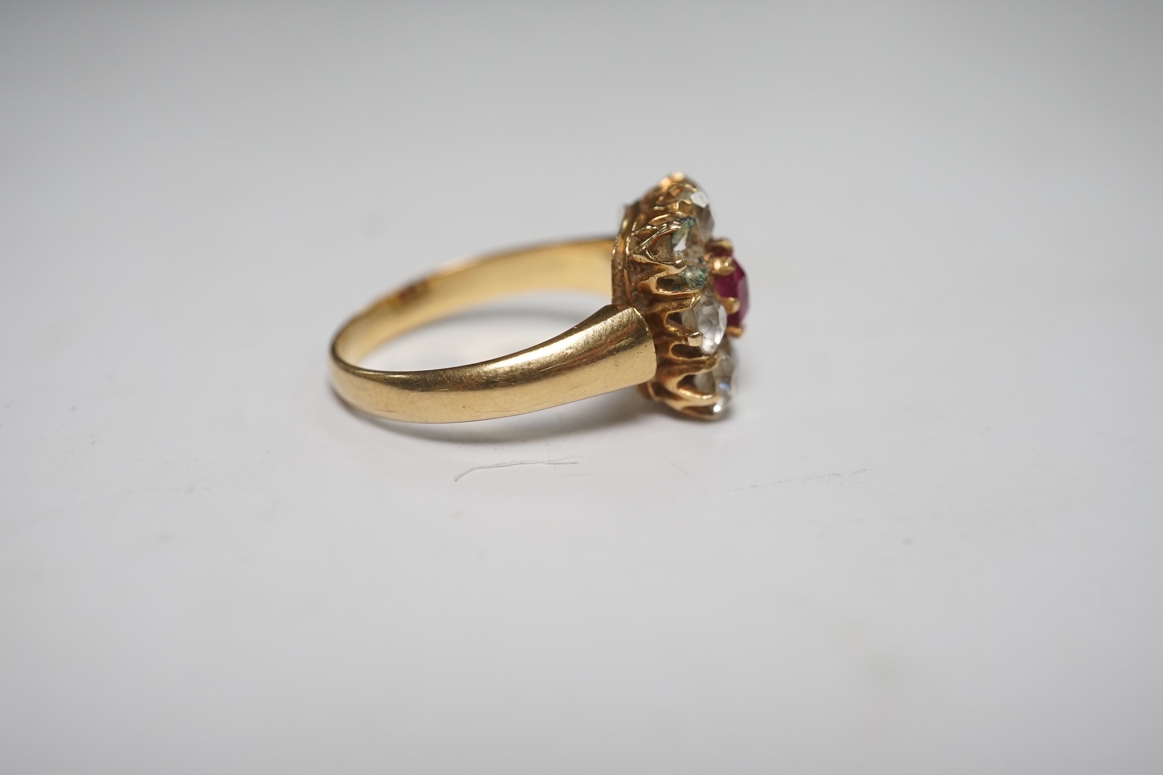 An early 20th century yellow metal, single stone ruby and eight stone diamond set square cluster ring, size O, gross weight 5 grams, one diamond missing. Condition - poor to fair